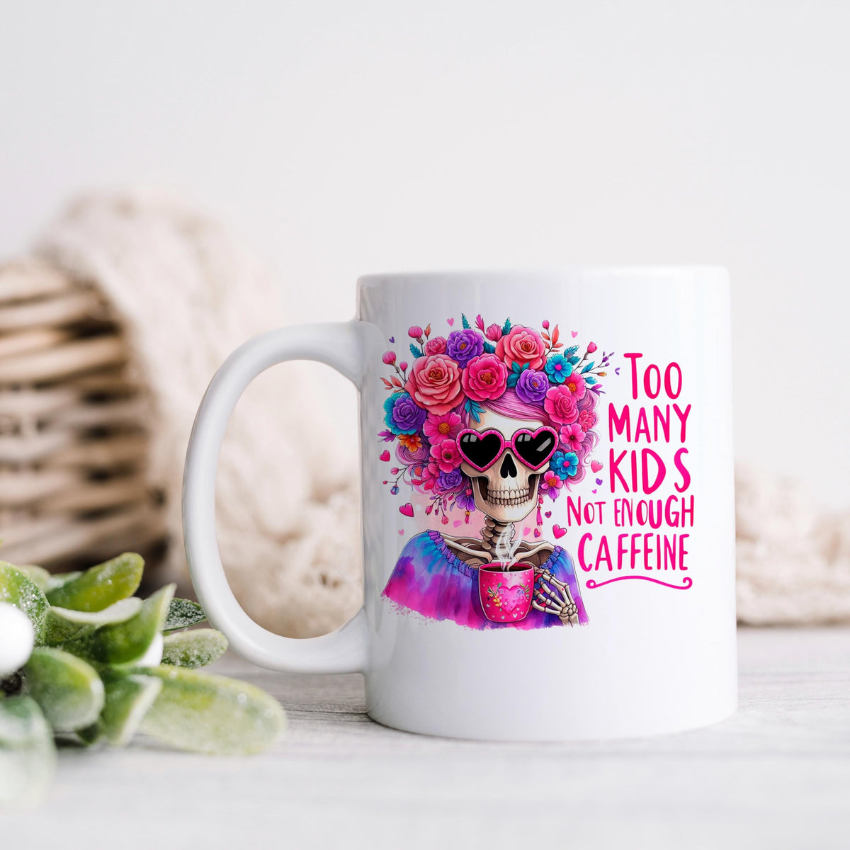 White ceramic mug with heart-sunglasses skull in a colorful flower crown and pink quote text.