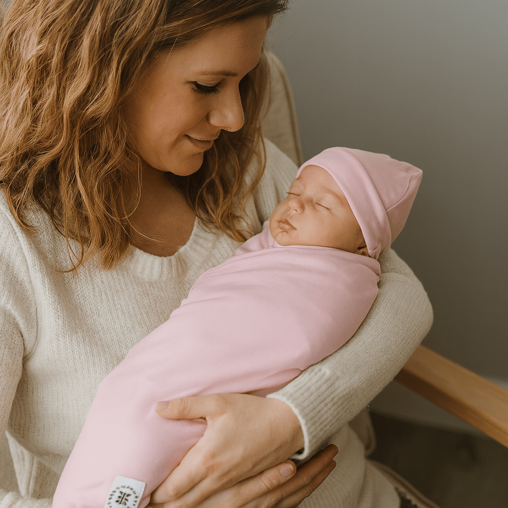 Pink swaddle blanket with hooded fold and small fabric corner tag.
