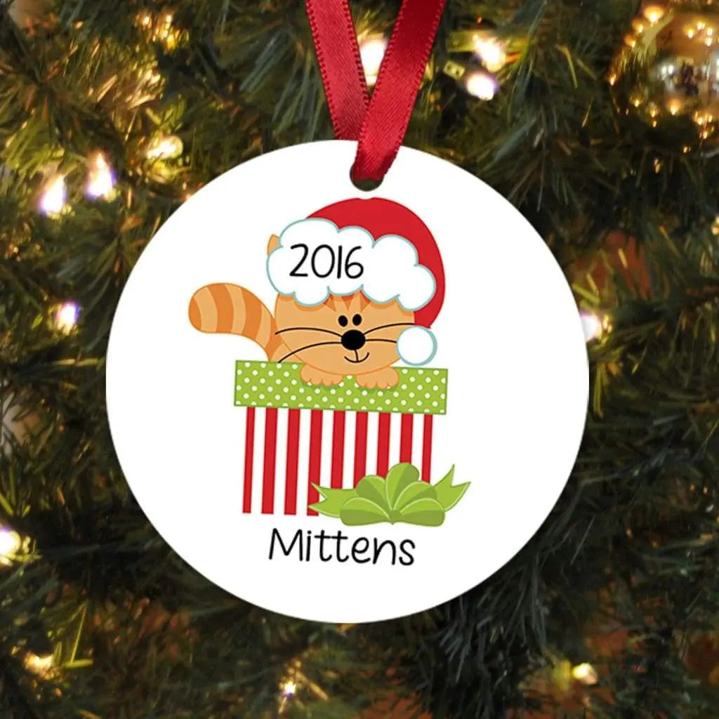 Round cat-themed Christmas ornament with red ribbon, 2016 and name “Mittens”