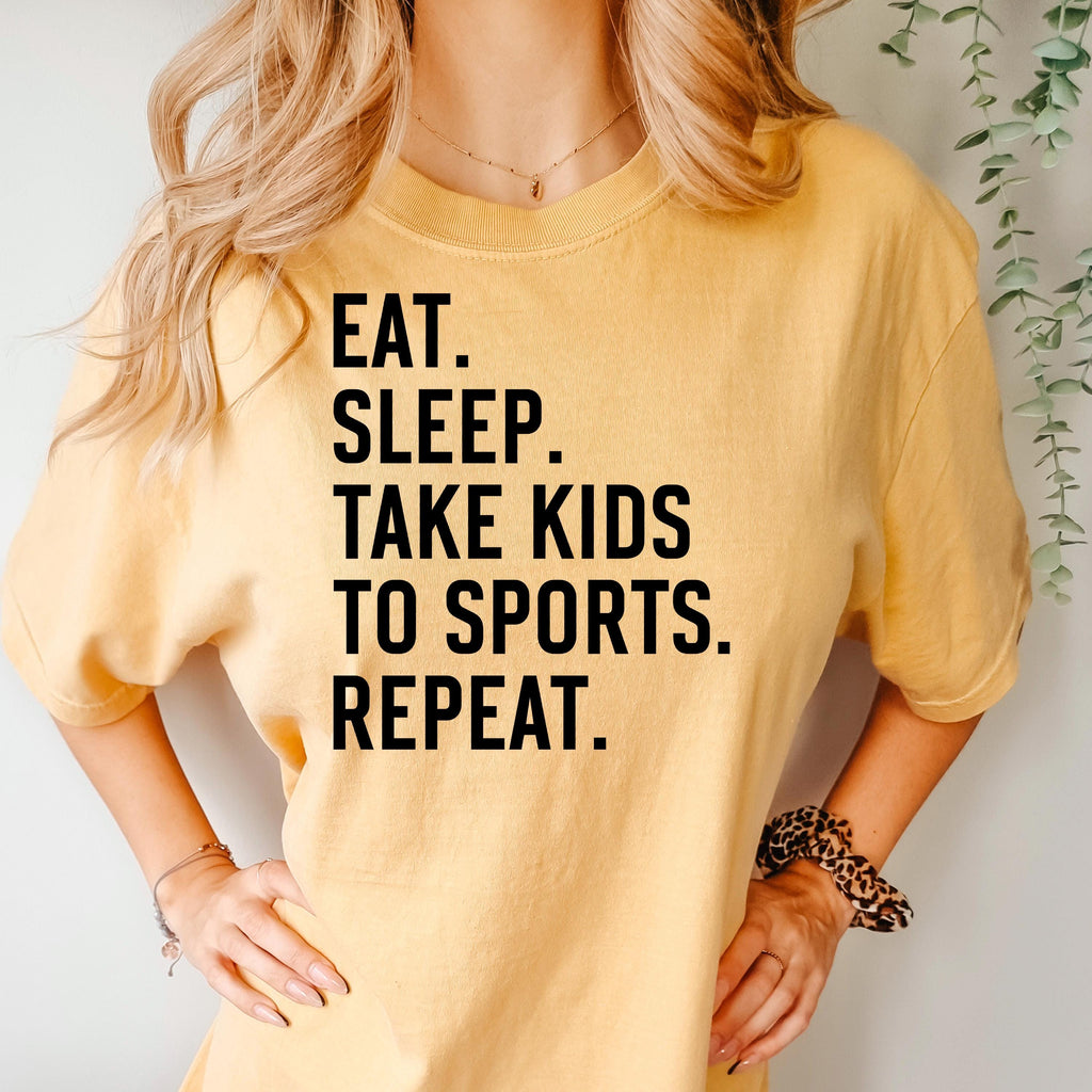 Mustard unisex graphic tee with black text: EAT SLEEP TAKE KIDS TO SPORTS REPEAT.