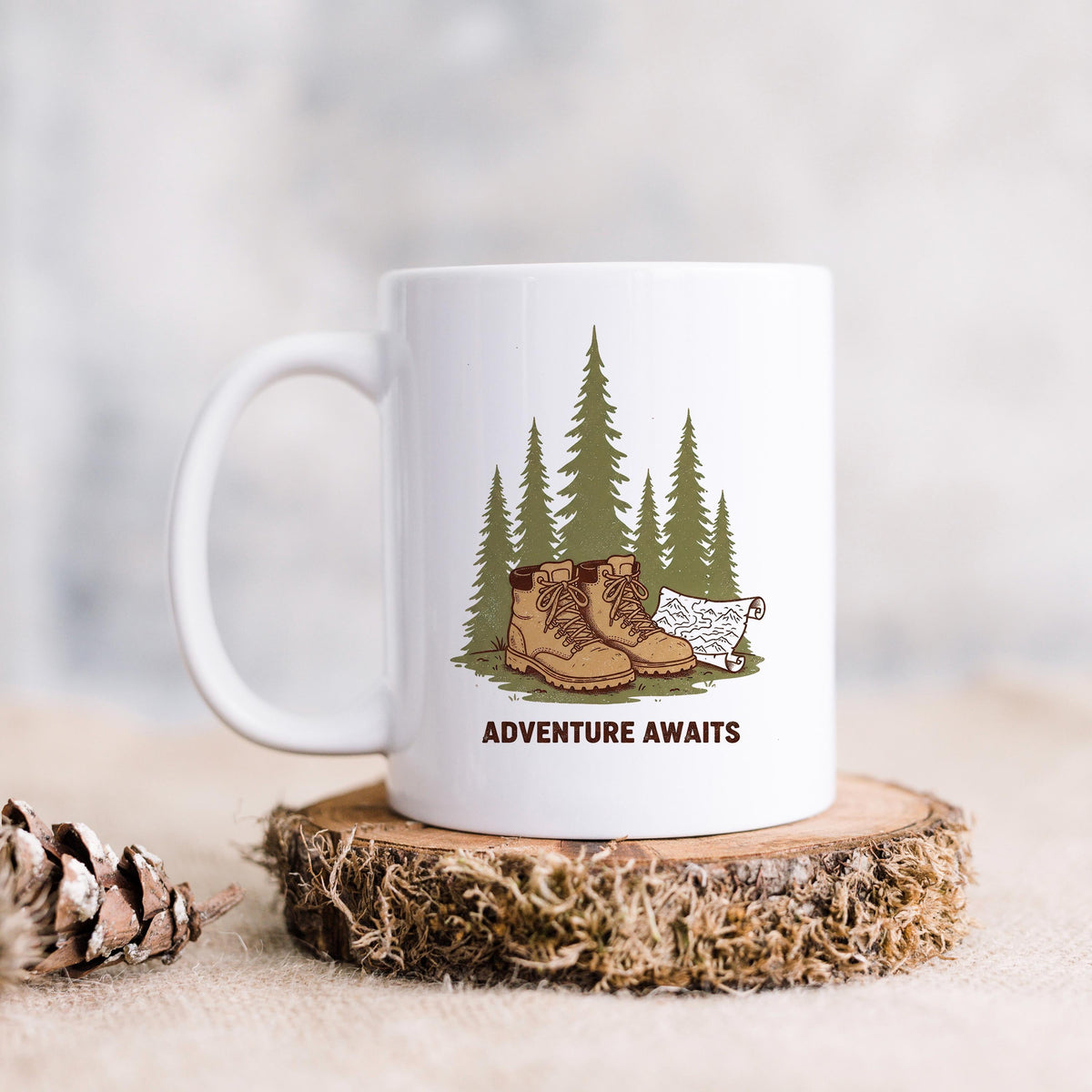 White ceramic hiking mug with 'ADVENTURE AWAITS' graphic: boots, pine trees, dog