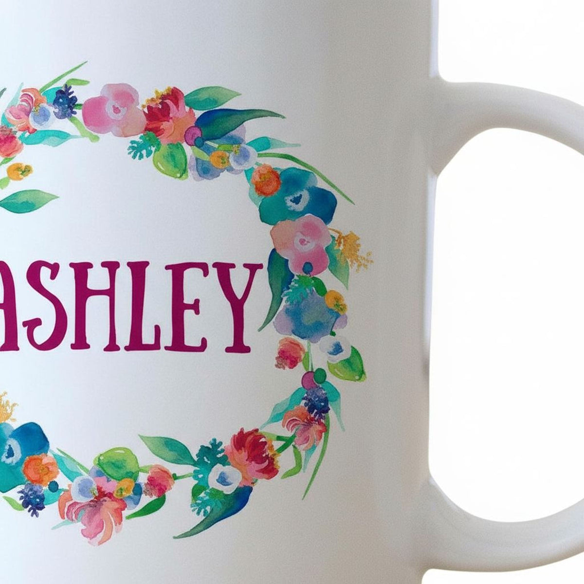 Close-up of white mug showing "ASHLEY" text inside a colorful floral wreath