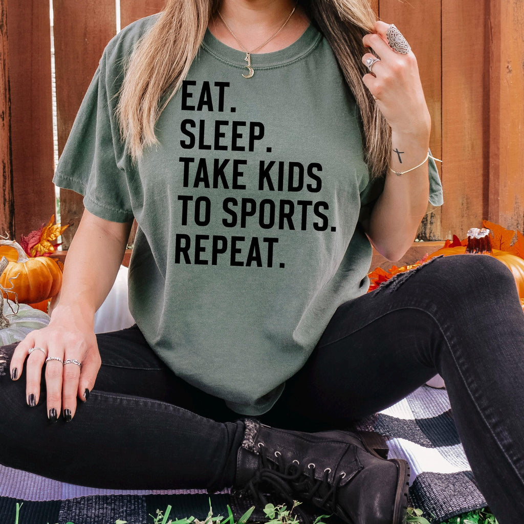 Dark green unisex graphic tee with black text: EAT SLEEP TAKE KIDS TO SPORTS REPEAT.