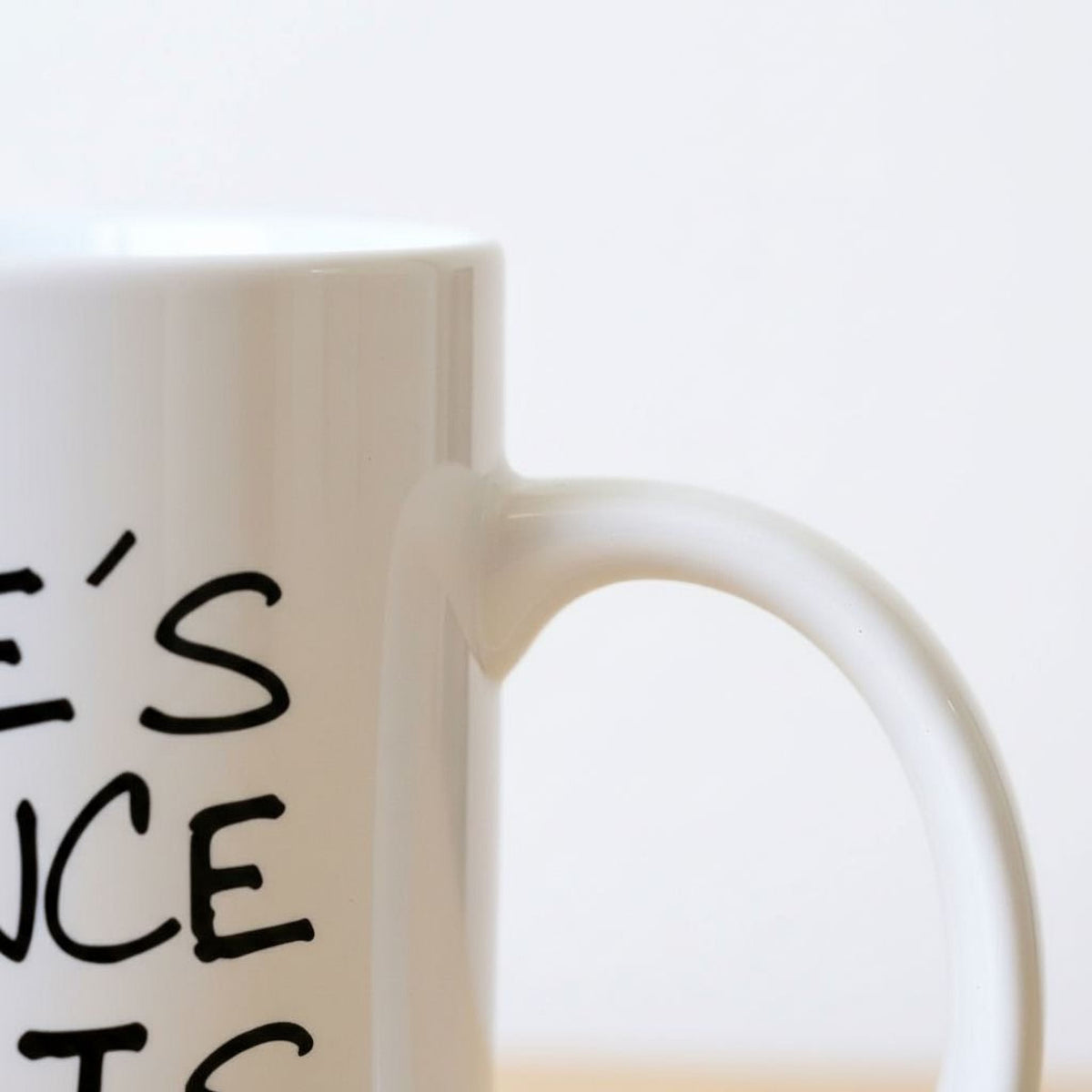 White ceramic coffee mug close-up of handle and partial printed quote.