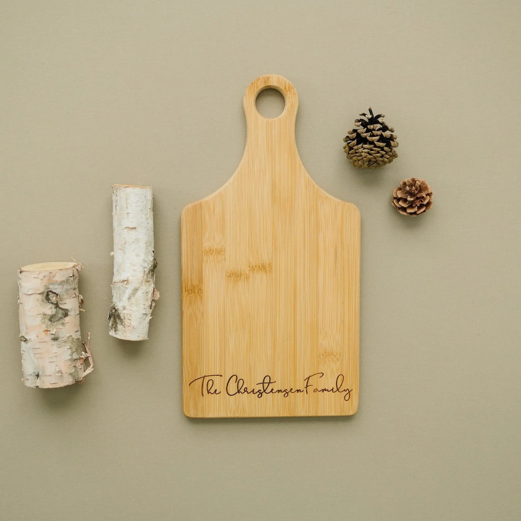 Wood charcuterie serving board with engraved "The Christen" family text and handle hole.