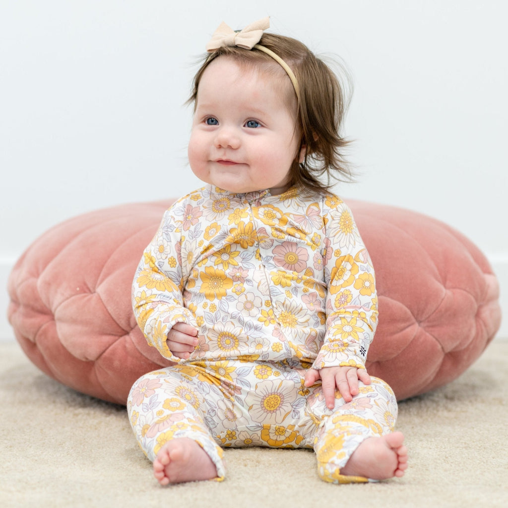 Infant floral long-sleeve romper in pastel yellow, pink, and white; baby sitting