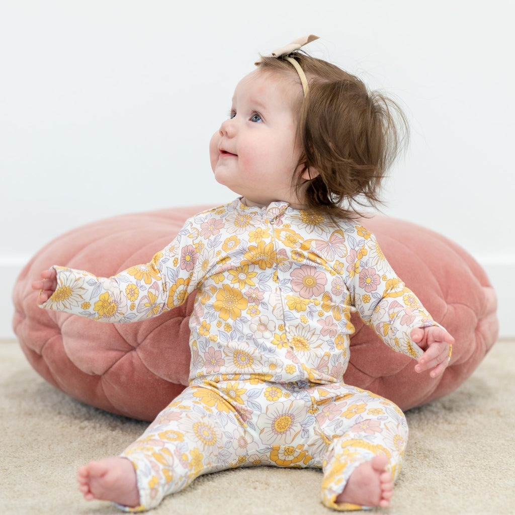 Infant floral long-sleeve romper in pastel yellow and pink daisies; baby seated