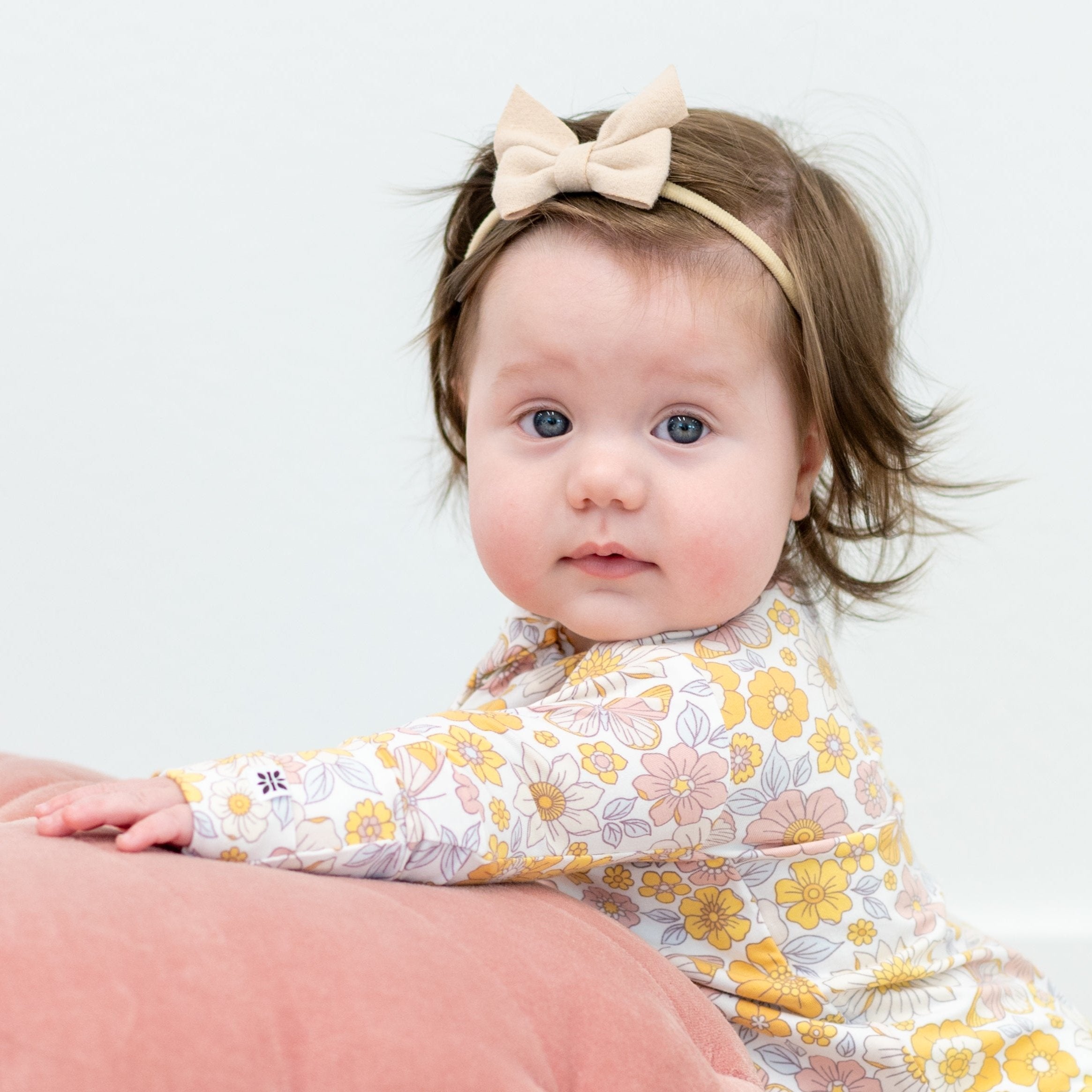 Infant floral long-sleeve romper in pastel yellow, pink, and white; worn with headband bow
