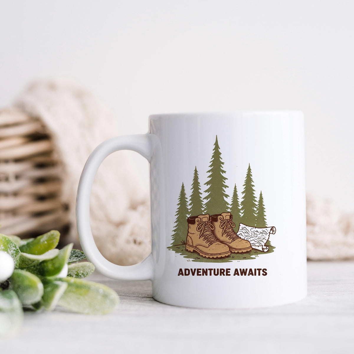 White ceramic mug with 'ADVENTURE AWAITS' graphic of boots, pine trees, and dog