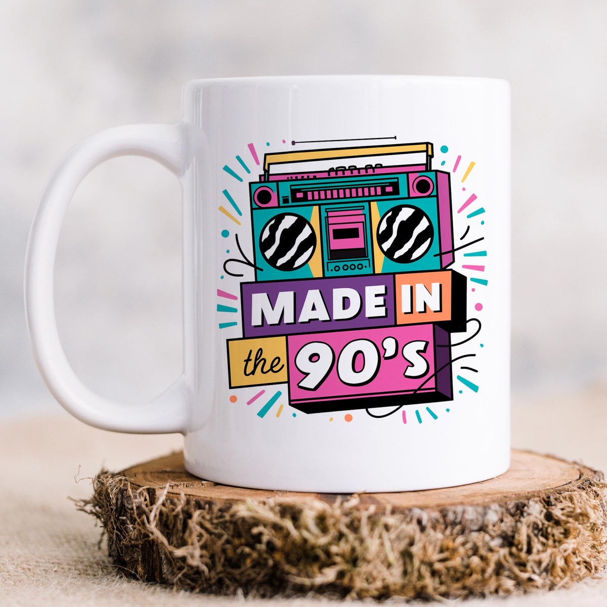 White ceramic mug with “Made in the 90’s” boombox graphic, on a wood slice
