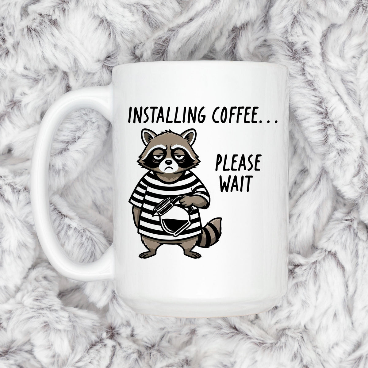 White ceramic coffee mug with cartoon raccoon and 'Installing coffee... Please wait' text.