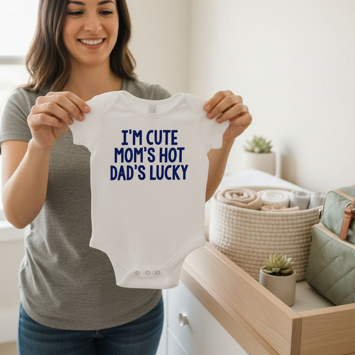 White newborn baby bodysuit with blue “I’m cute mom’s hot dad’s lucky” text