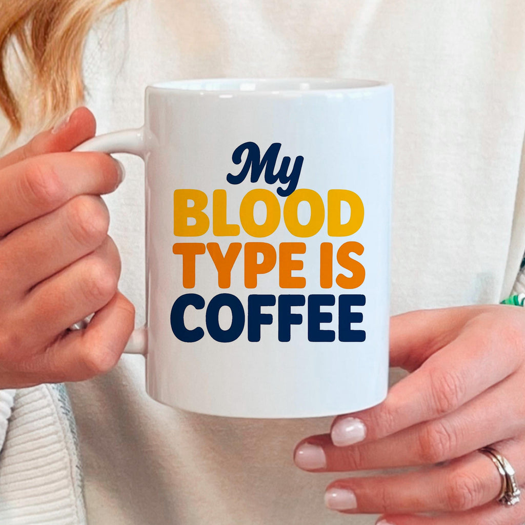 White ceramic coffee mug held in hands, “My BLOOD TYPE IS COFFEE” text visible.