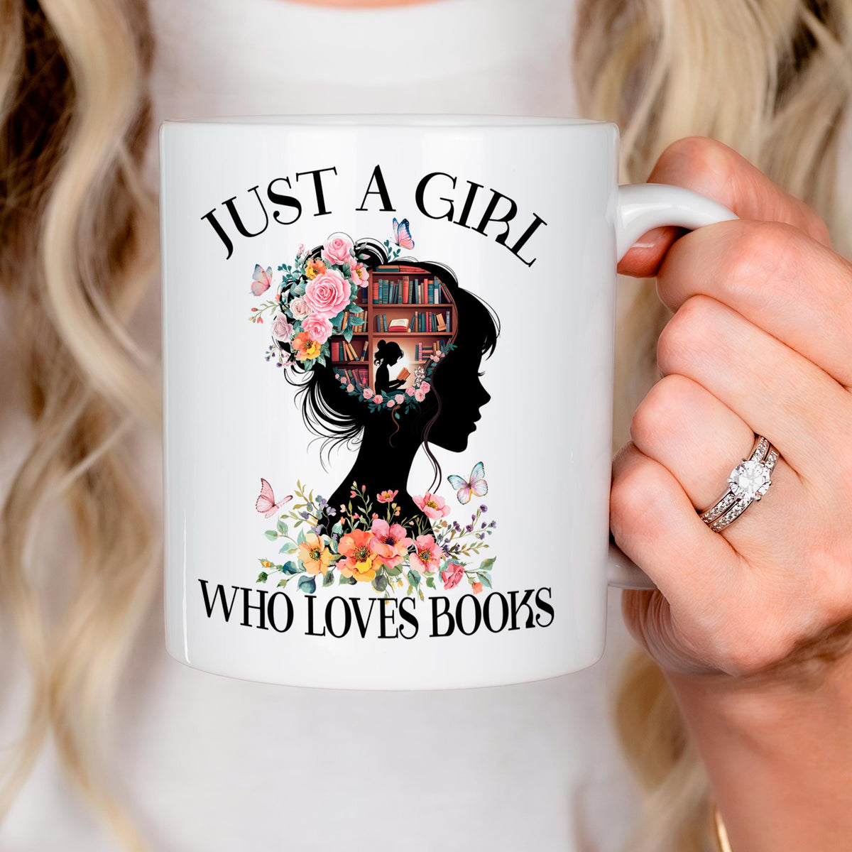 White ceramic coffee mug held in hand with floral book silhouette and “WHO LOVES BOOKS” text.
