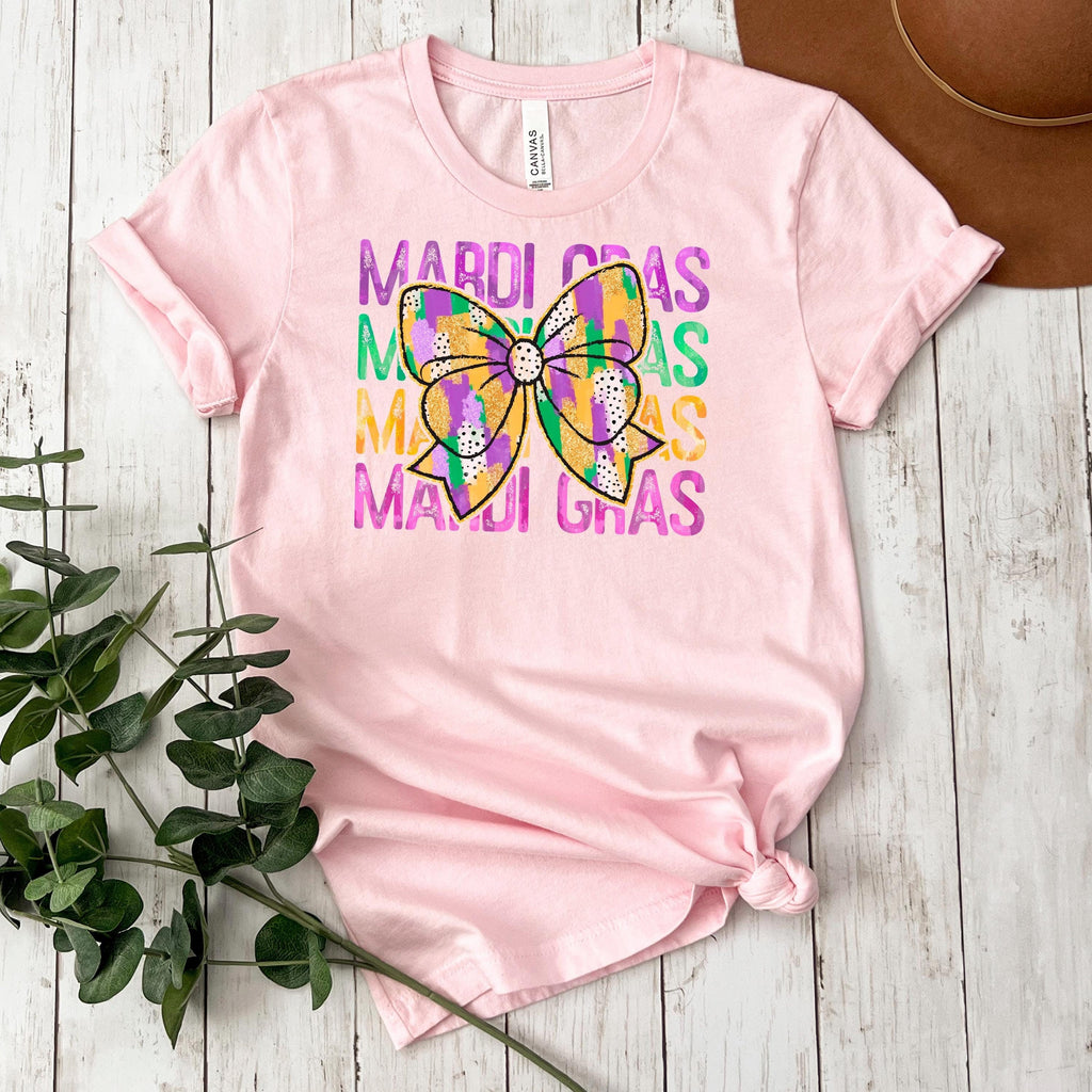Pink short-sleeve t-shirt with Mardi Gras bow and colorful stacked text graphic