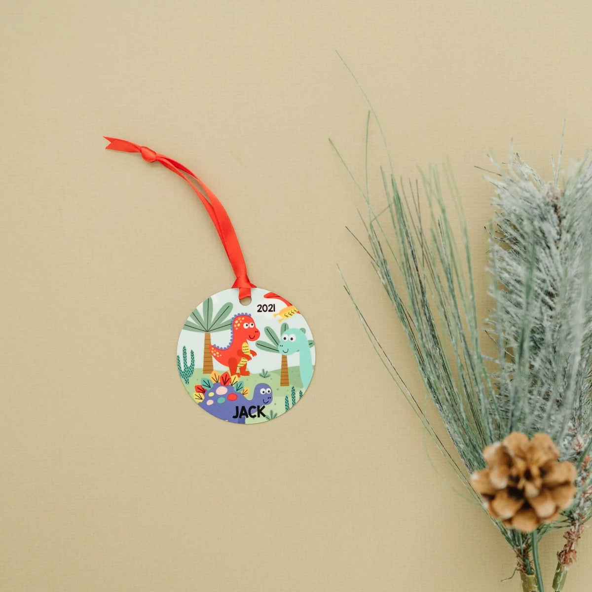 Round dinosaur ornament with red string, '2021' and 'JACK' text on scenic background