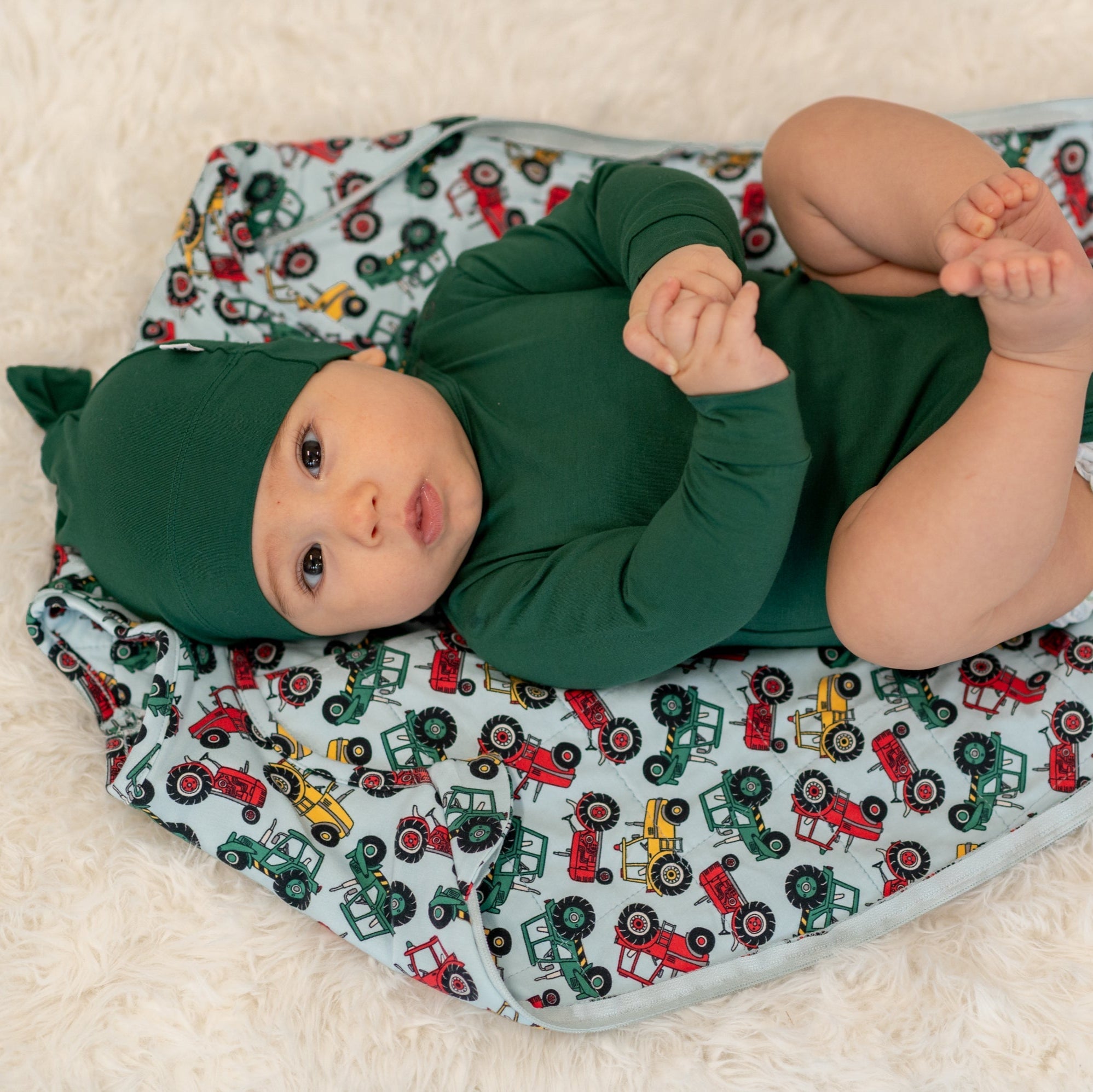 Sleep sack with multicolor tractor print and dark green sleeve panels, baby lying