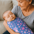 Swaddle blanket swirled with purple, pink flowers and bird motifs, folded around a baby