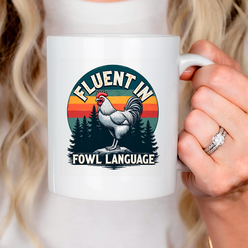 White ceramic mug close-up with rooster graphic and “FLUENT IN FOWL LANGUAGE” text