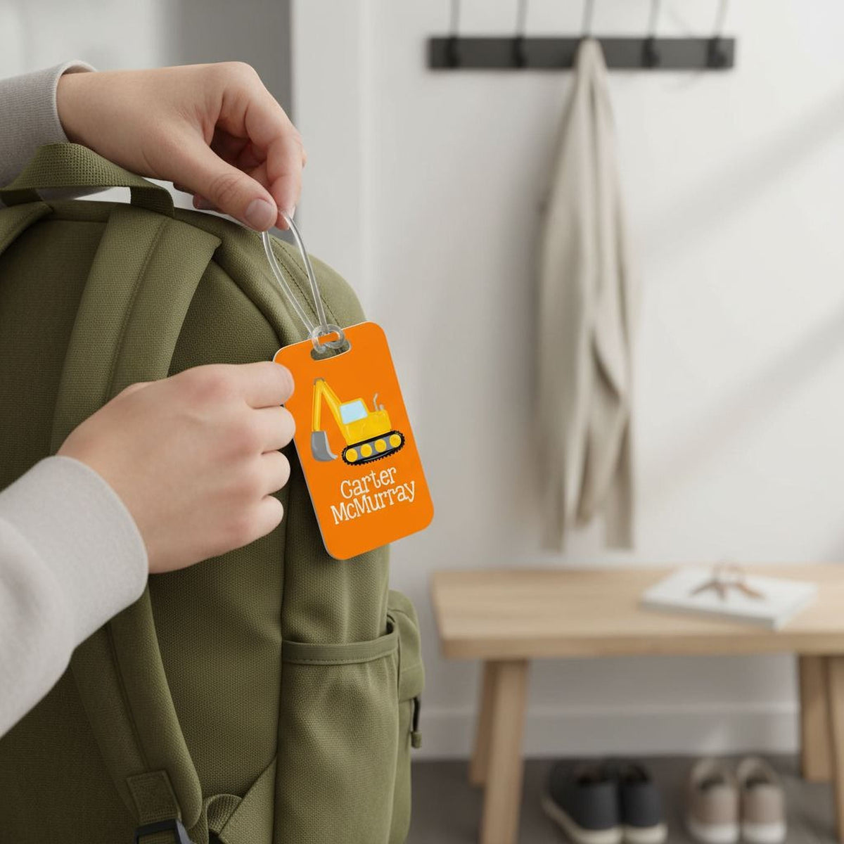 Boys backpack name tag on orange card attached to an olive backpack, held by hand