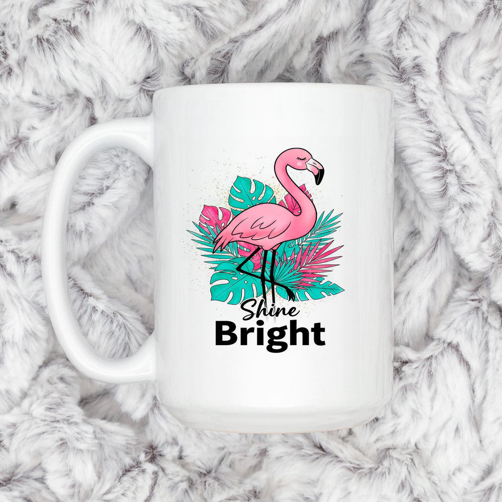 White mug on plush fabric, featuring pink flamingo, tropical leaves, and “Shine Bright”