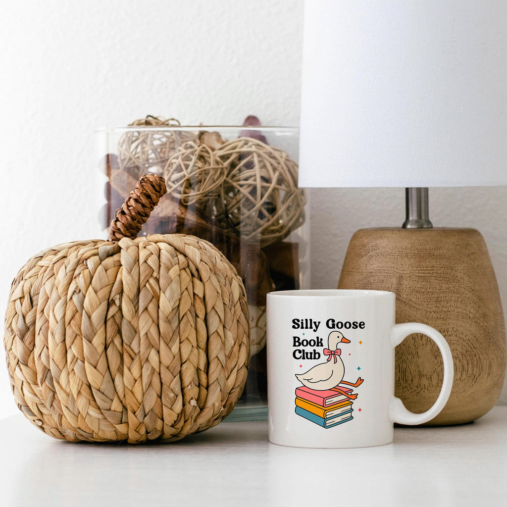 White ceramic mug with cartoon goose on stacked books, 'Silly Goose Book Club' text.