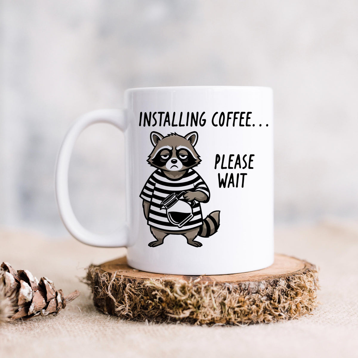 White ceramic coffee mug with cartoon raccoon and 'Installing coffee... Please wait' graphic.