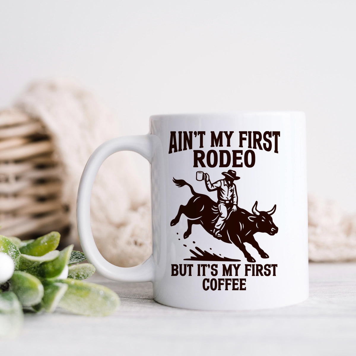 White ceramic coffee mug with rodeo graphic and “But it’s my first coffee” text.