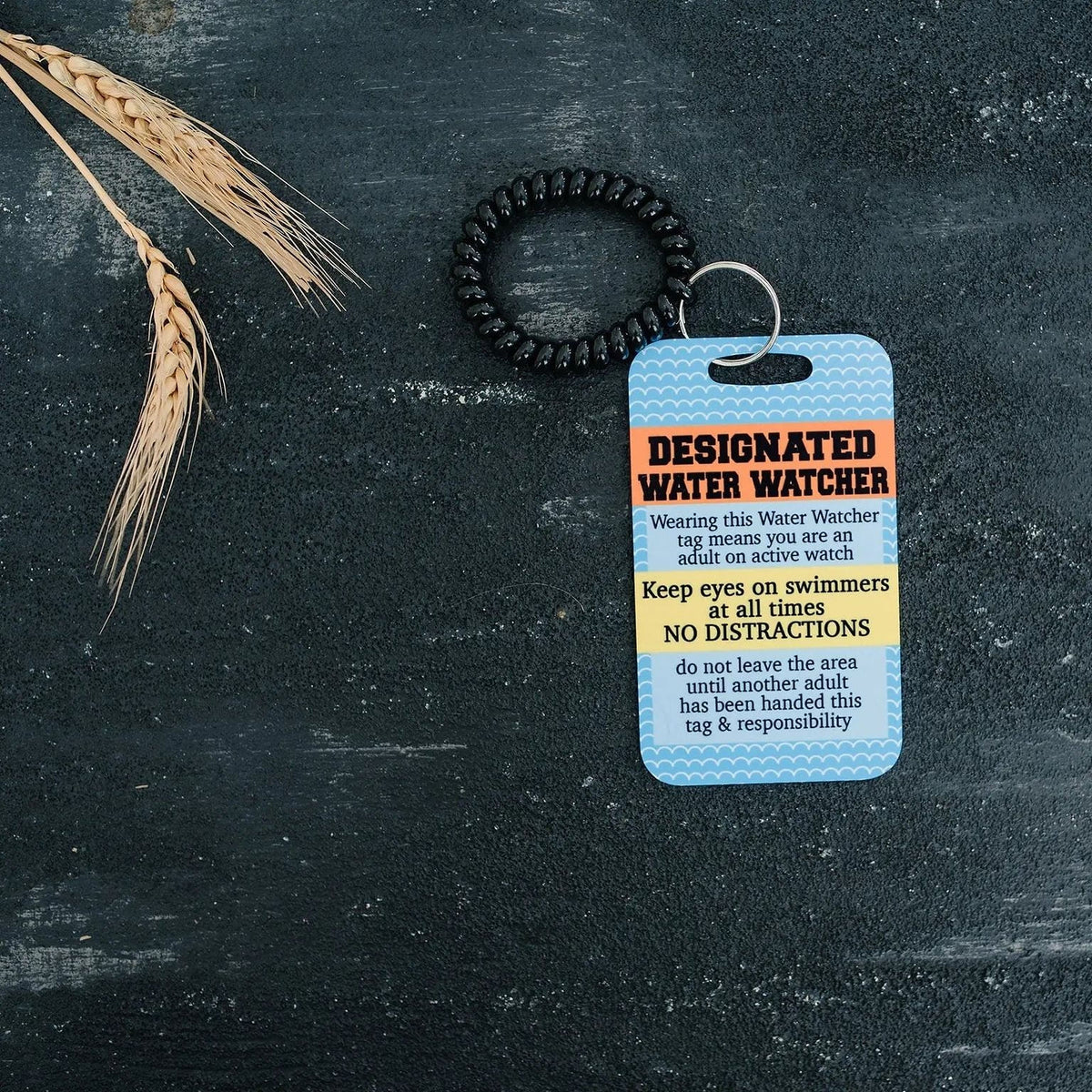 Pool safety badge tag with black beaded lanyard and blue card on dark surface