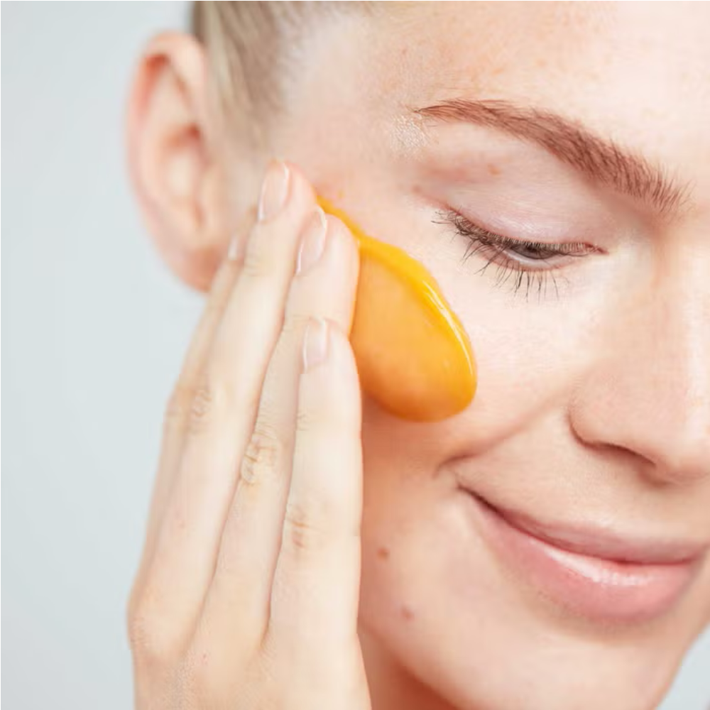 Orange cleansing butter applied under eye by fingertips