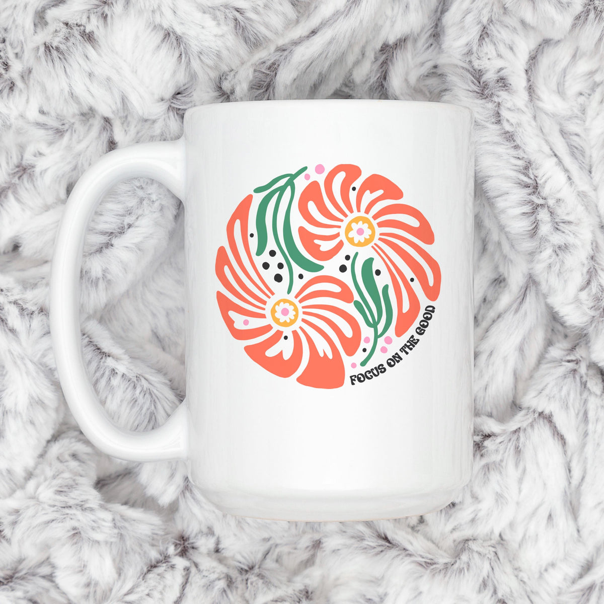 White ceramic mug with coral floral design and green leaves, top view on soft fur