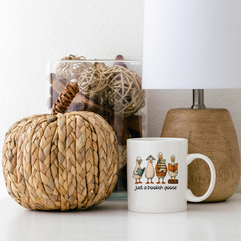 White ceramic coffee mug with bookish geese graphic and "just a bookish goose"