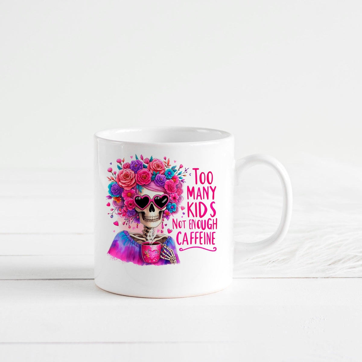White ceramic mug standing alone with colorful floral crown skull and “Too Many Kids” coffee saying.