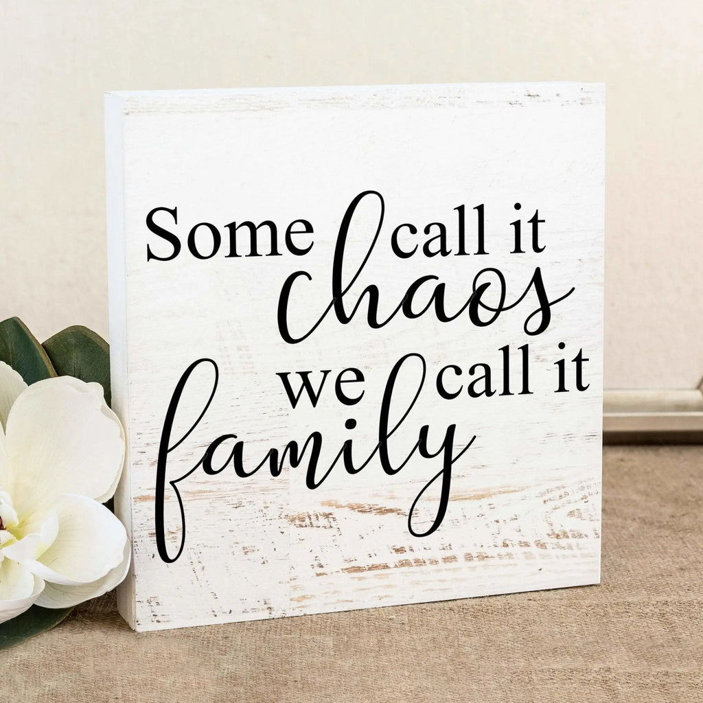White wooden wall sign with black cursive quote: Some call it chaos, we call it family.