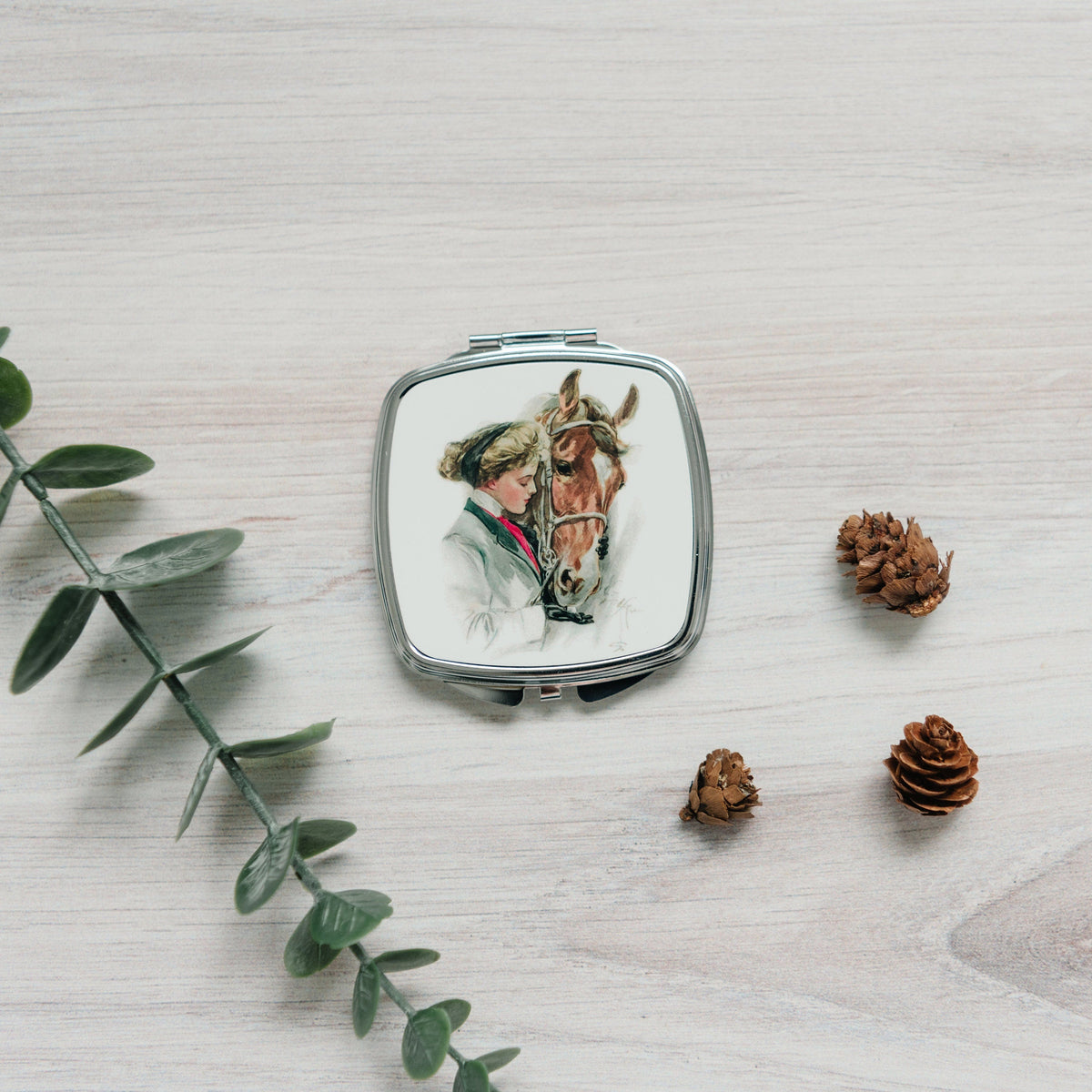 Square silver compact mirror with horse portrait illustration centered on the front lid