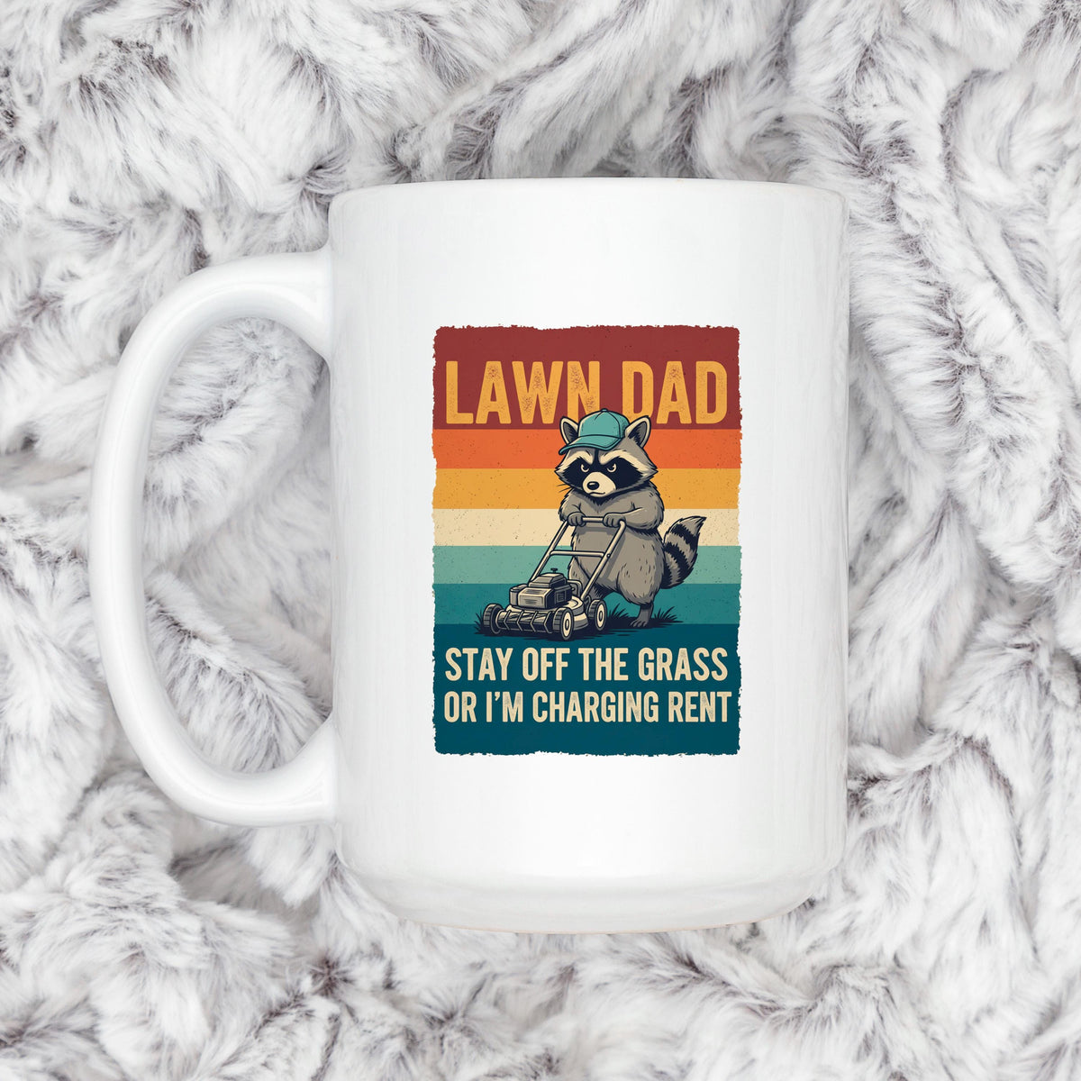 White coffee mug with raccoon mowing graphic and slogan “STAY OFF THE GRASS”