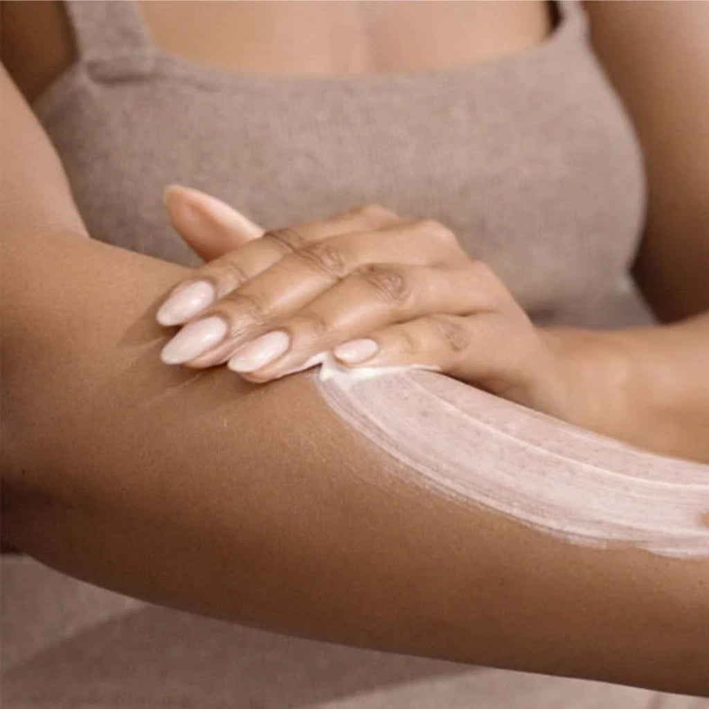 White body lotion spread on forearm with fingertips, skincare application