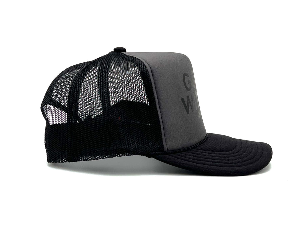 Charcoal foam trucker cap with black mesh sides and curved brim; side lettering visible.