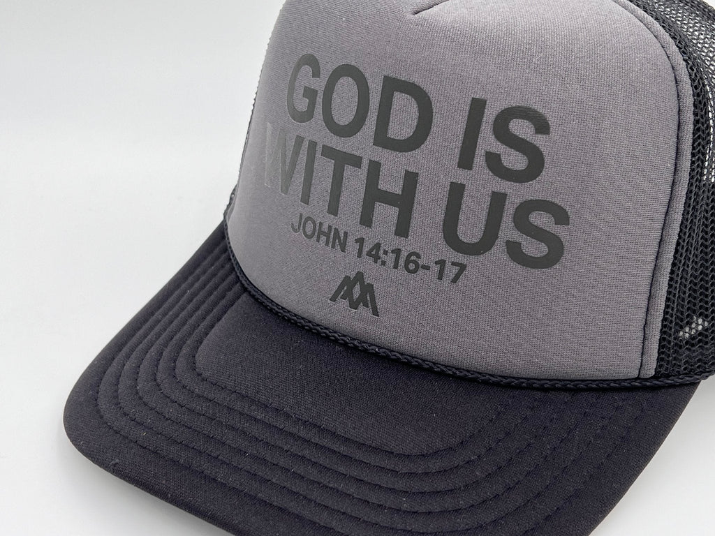 Charcoal foam trucker cap close-up: “GOD IS WITH US” with “JOHN 14:16-17” on front.