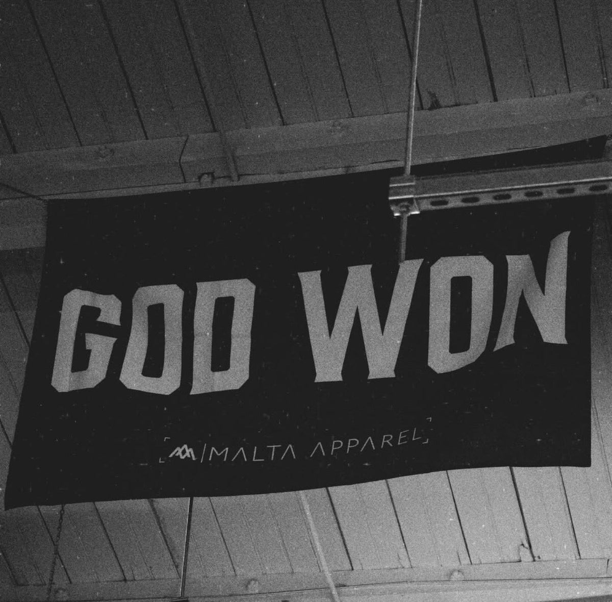 Black flag on pole with large white 'GOD WON' lettering and Malta Apparel mark