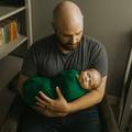 Hunter green baby swaddle blanket wrapped around infant in arms, corner visible