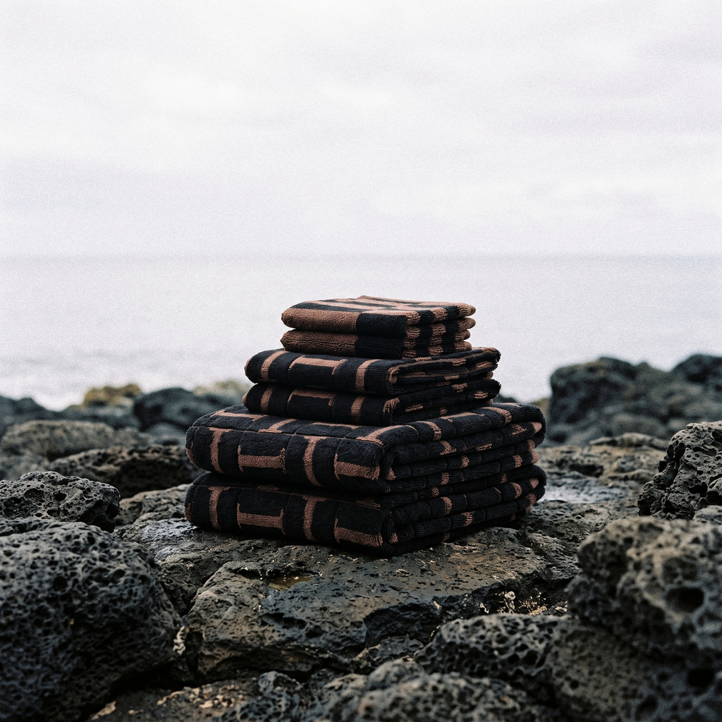 Stack of folded cotton towels in tobacco brown and black plaid stripe pattern on rocks