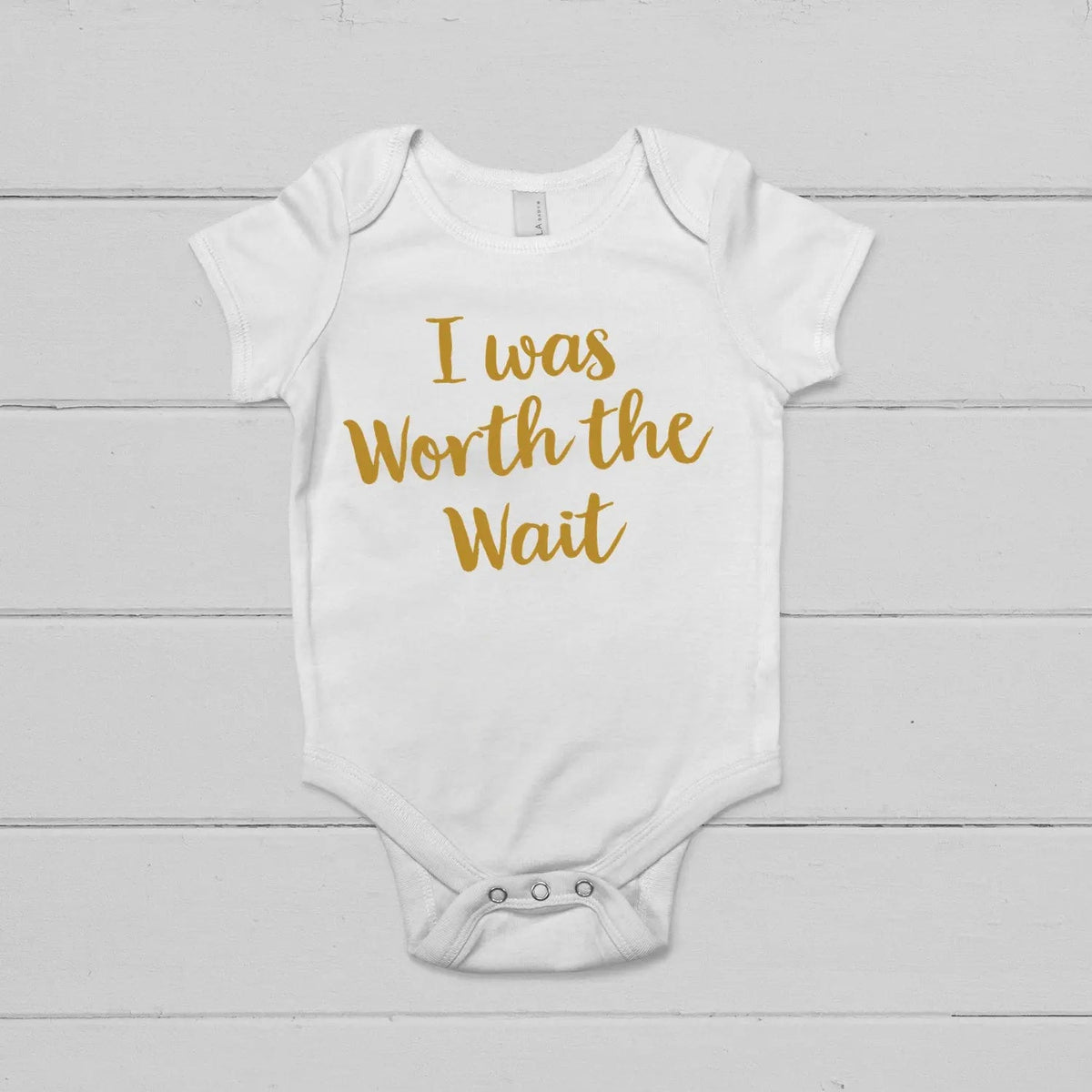White short-sleeve snap onesie with gold 'I was Worth the Wait' lettering