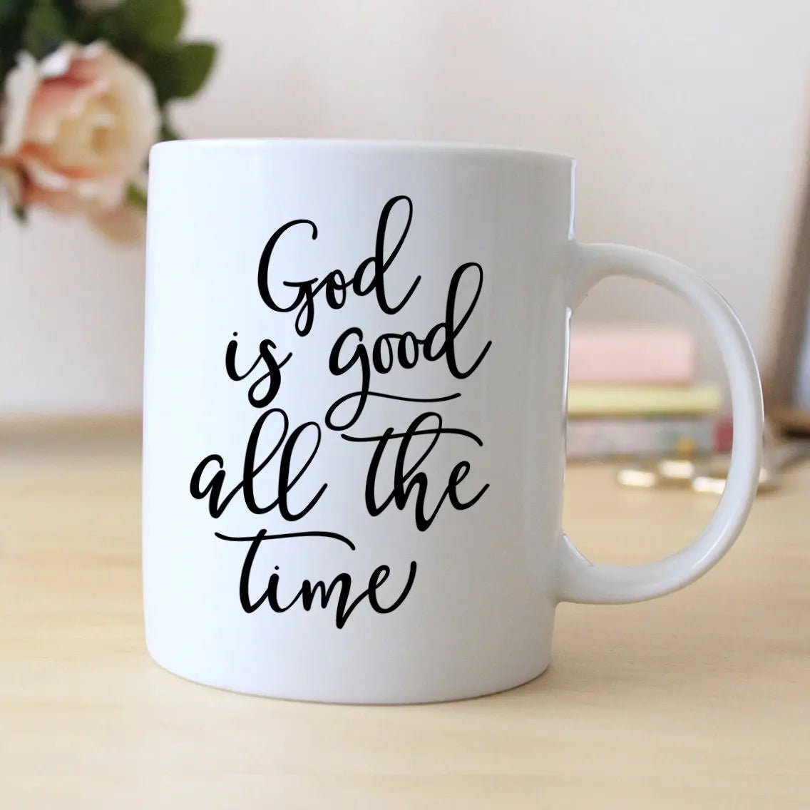 White ceramic coffee mug with 'God is good all the time' script, handle visible