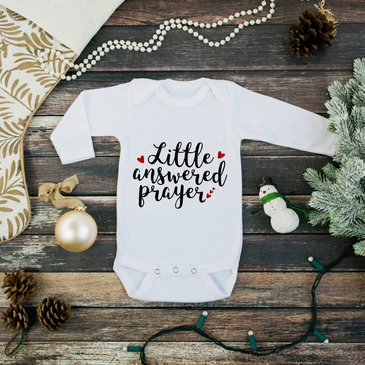 White long-sleeve baby bodysuit with “Little answered prayer” print.