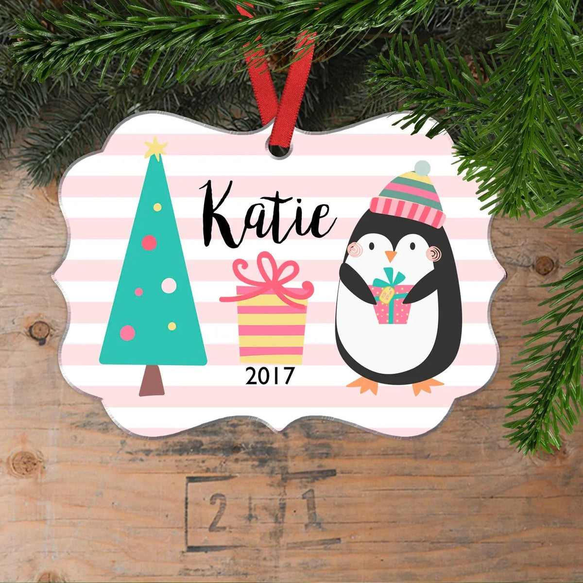 Pink striped Christmas ornament with penguin, tree, gift, and name Katie
