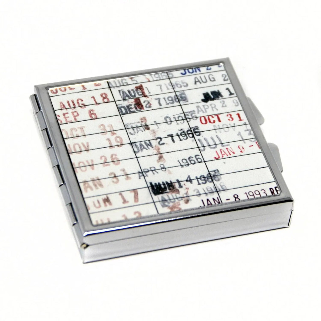 Square metal pill box with hinged lid, open to calendar-style date print