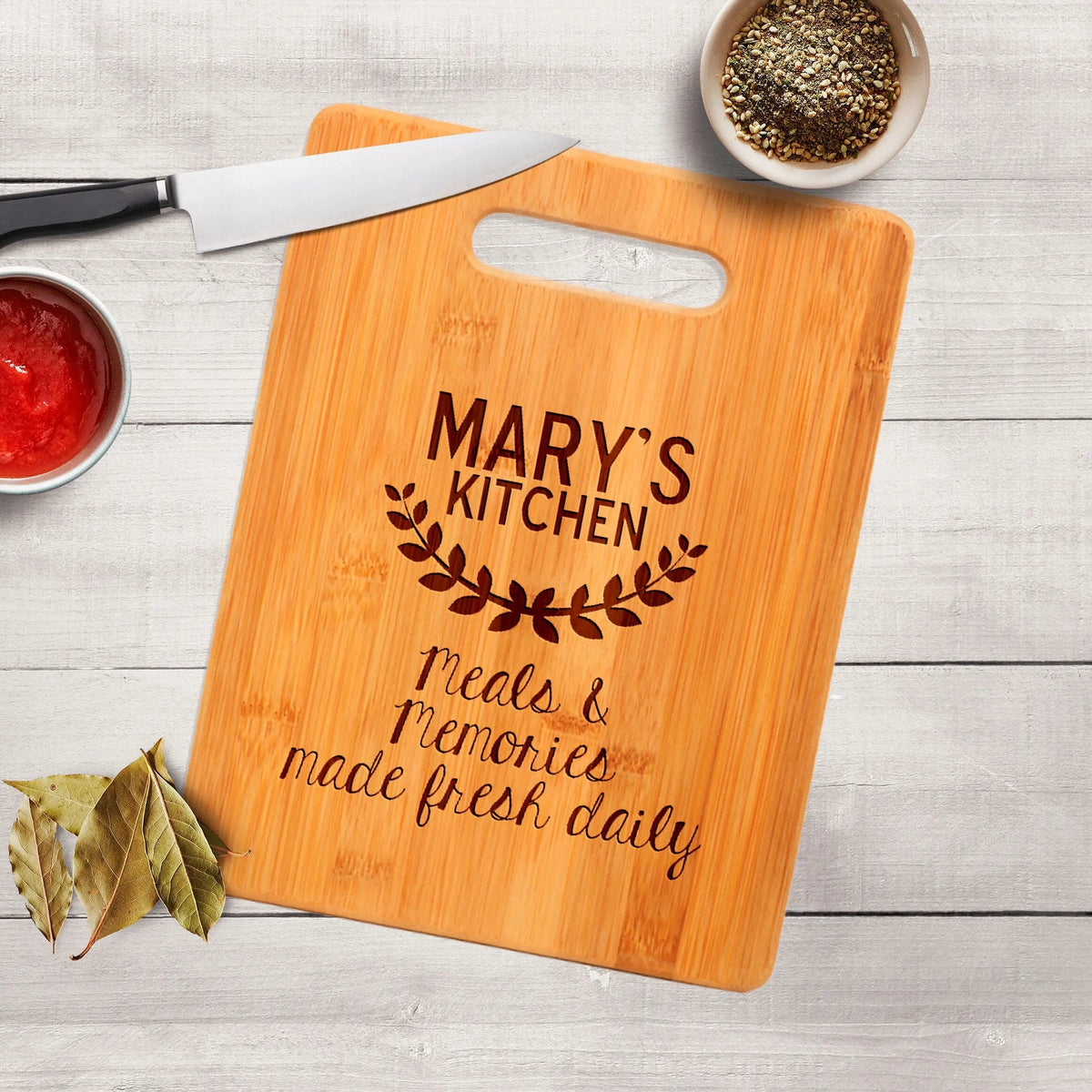 Wood cutting board with handle cutout and engraved “MARY’S KITCHEN”