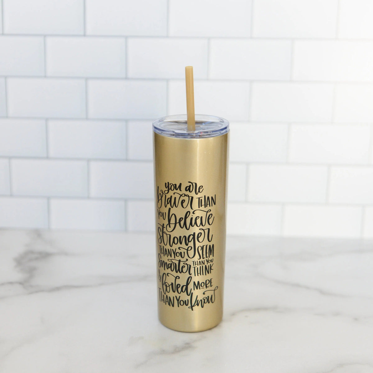 Gold glitter skinny tumbler with straw and black motivational quote, standing upright