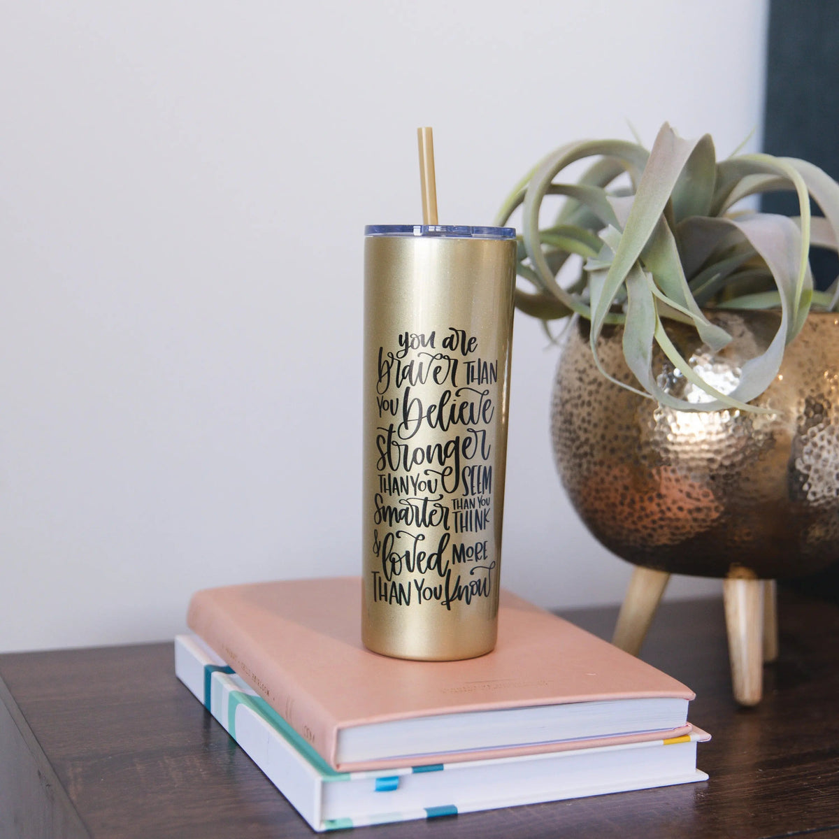 Gold glitter skinny tumbler with straw and black motivational quote, on a desk